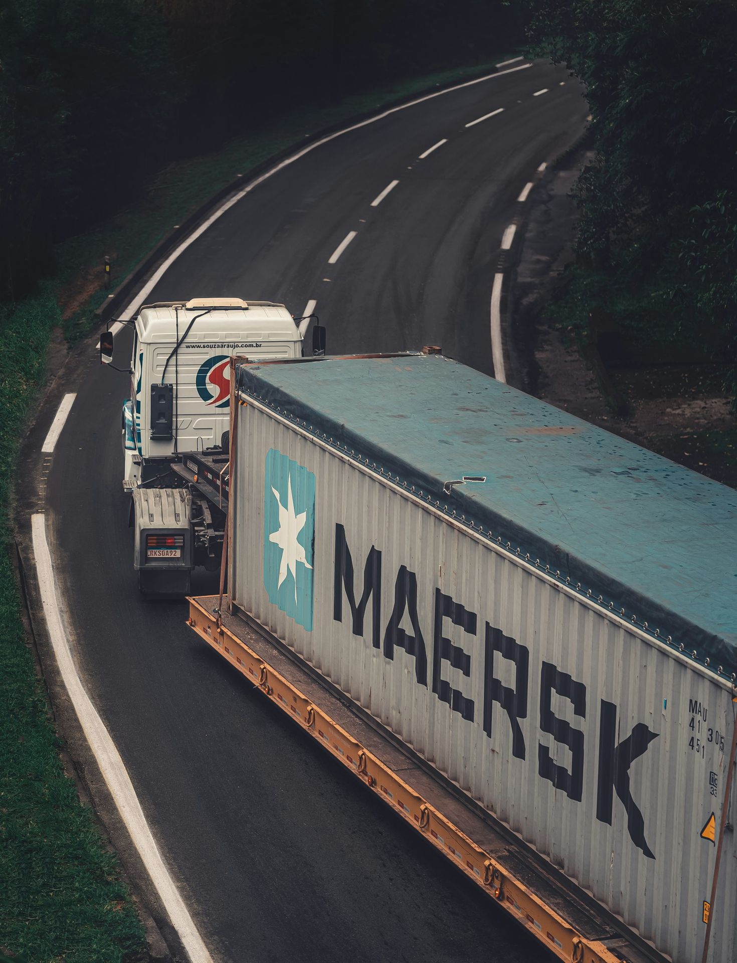 a semi truck driving down a road next to a forest